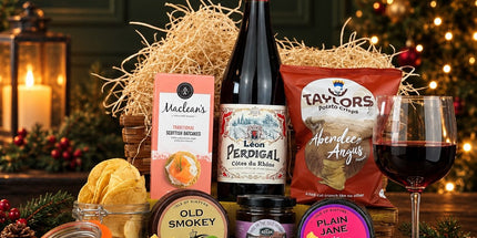 Christmas wine and cheese hamper with Scottish cheese, oatcakes, chutney and crisps beside a lit Christmas tree.