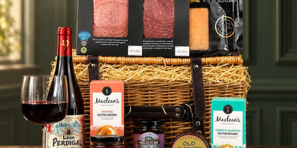 Scottish red wine hamper with smoked beef, venison, cheese, oatcakes and chutney in front of a wicker basket.