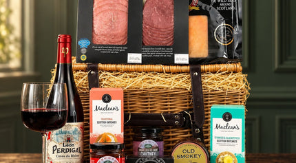 Scottish red wine hamper with smoked beef, venison, cheese, oatcakes and chutney in front of a wicker basket.