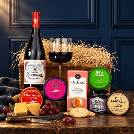 Red wine and cheese hamper with Scottish cheese truckles, oatcakes and chutney in front of an open wicker basket.