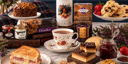Scottish afternoon tea hamper with tea, fruit cake, preserves, scones, cake slices and sweet treats on a marble table.