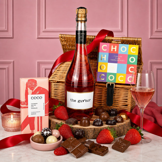 Gourmet gift basket with wine, chocolates, and strawberries on a pink background