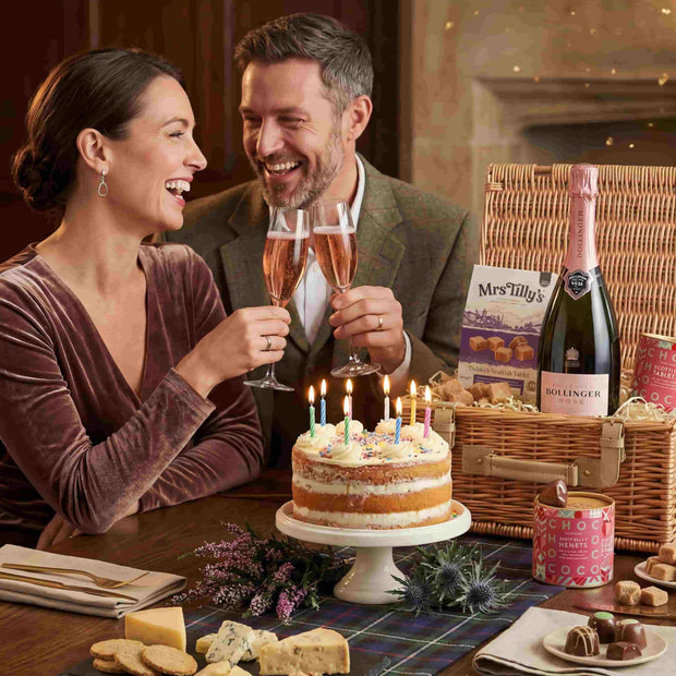 Couple celebrating with a cake and champagne in a cozy room.